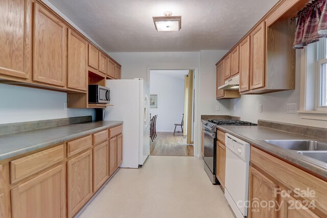 kitchen featuring light wood-type flooring, a textured ceiling, white appliances, and light brown cabinetry