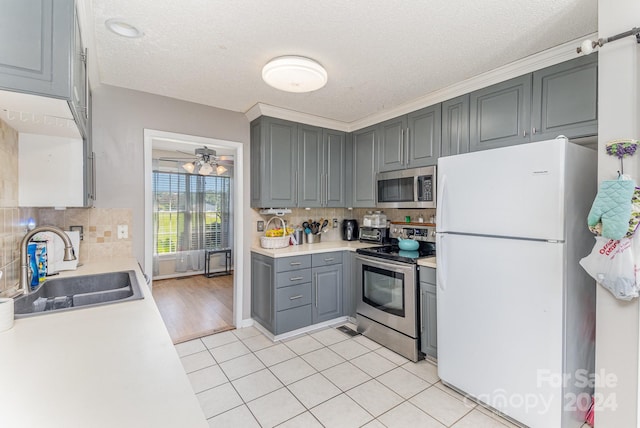 kitchen featuring sink, gray cabinets, a textured ceiling, light tile patterned flooring, and stainless steel appliances