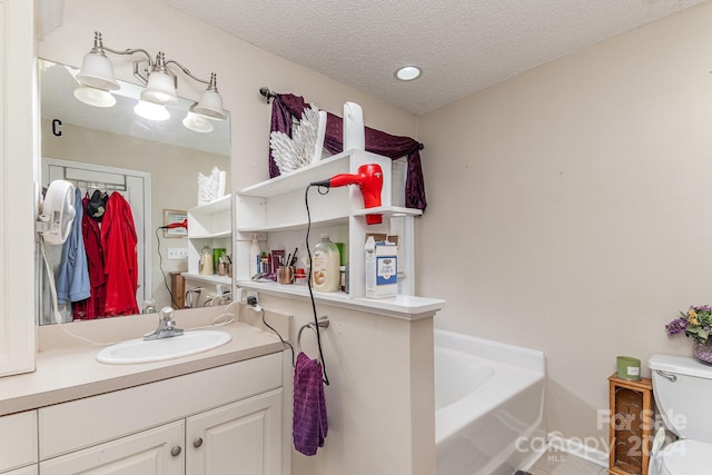 bathroom featuring a bathing tub, vanity, toilet, and a textured ceiling