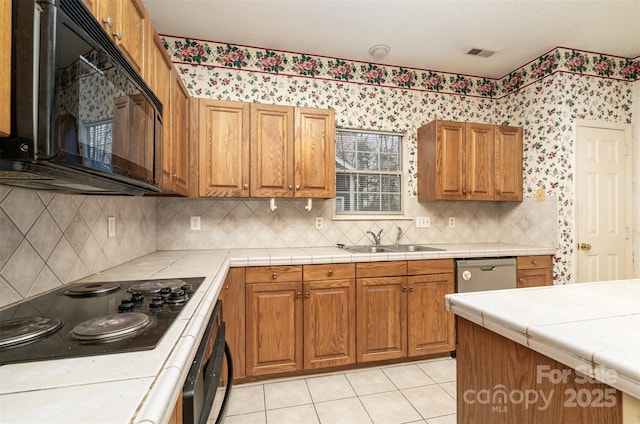 kitchen featuring light tile patterned flooring, tile counters, black appliances, and sink