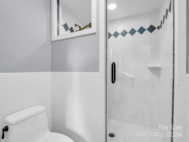 bathroom featuring a shower with door, tile walls, and toilet