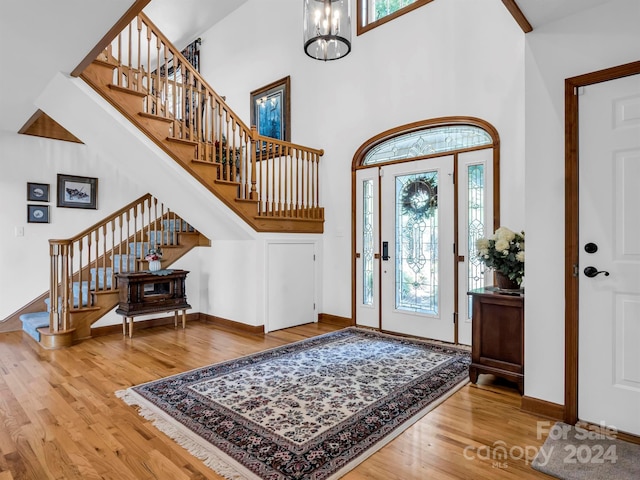 foyer entrance with hardwood / wood-style floors, high vaulted ceiling, and a notable chandelier