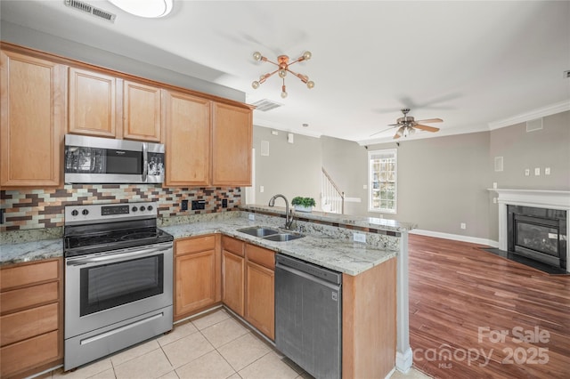 kitchen featuring ceiling fan, sink, stainless steel appliances, kitchen peninsula, and ornamental molding