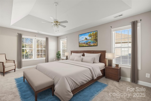 bedroom with a tray ceiling, multiple windows, ceiling fan, and light carpet