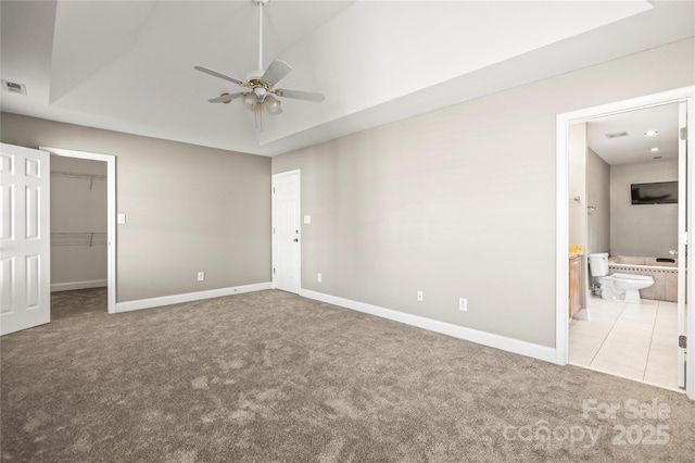 unfurnished bedroom featuring connected bathroom, a tray ceiling, a spacious closet, and ceiling fan