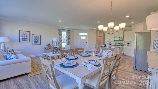 dining room featuring ornamental molding, sink, a chandelier, and light hardwood / wood-style flooring