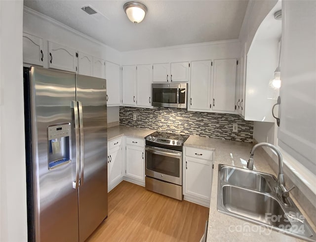 kitchen featuring appliances with stainless steel finishes, light hardwood / wood-style floors, tasteful backsplash, sink, and white cabinets