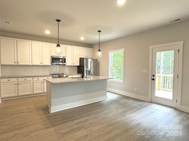 kitchen with white cabinets, appliances with stainless steel finishes, a kitchen island with sink, and hanging light fixtures