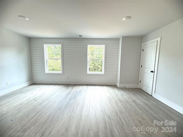 empty room featuring wood walls, plenty of natural light, and light wood-type flooring