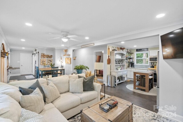 living room featuring ornamental molding, hardwood / wood-style floors, ceiling fan, and a barn door