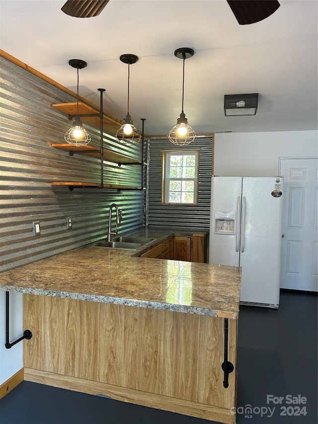 kitchen with a peninsula, white refrigerator with ice dispenser, pendant lighting, and a sink