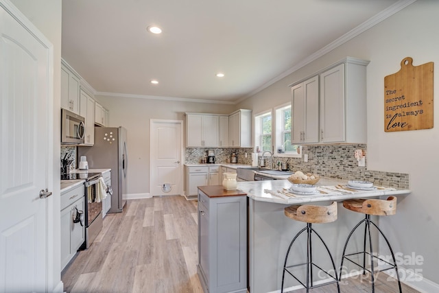 kitchen featuring a breakfast bar area, a peninsula, white cabinets, light countertops, and appliances with stainless steel finishes