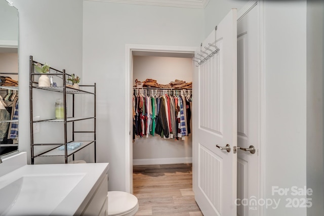 bathroom with toilet, wood finished floors, a sink, baseboards, and a walk in closet