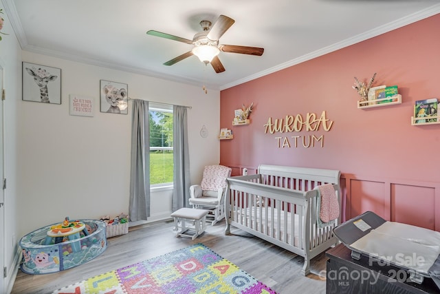 bedroom featuring a crib, light wood-style flooring, a ceiling fan, and crown molding