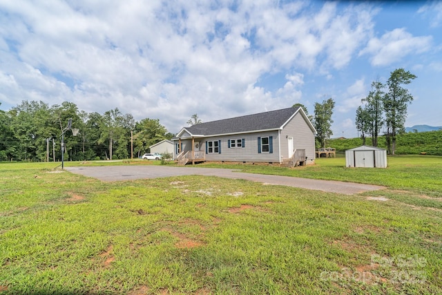 view of front of property featuring driveway, an outbuilding, crawl space, a shed, and a front lawn