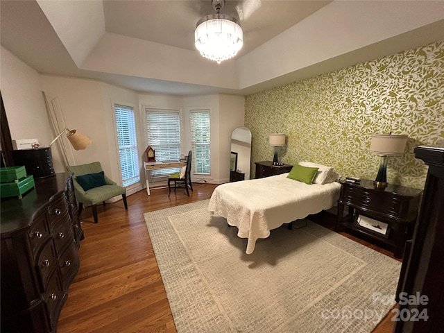 bedroom featuring a raised ceiling, dark hardwood / wood-style floors, and a notable chandelier