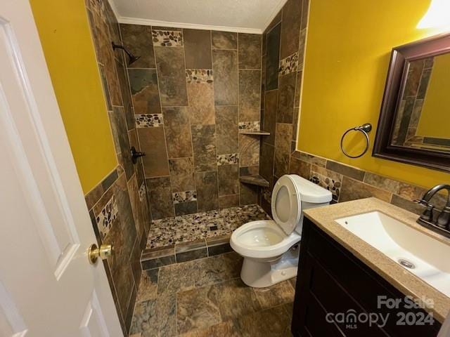 bathroom featuring a tile shower, tile walls, vanity, ornamental molding, and toilet