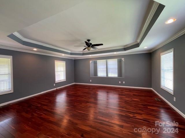 empty room featuring ceiling fan, a raised ceiling, hardwood / wood-style flooring, and crown molding