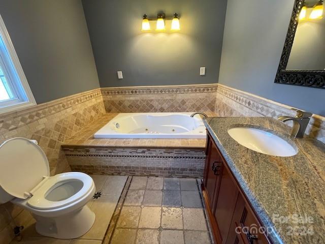 bathroom with toilet, vanity, tiled bath, and tile walls