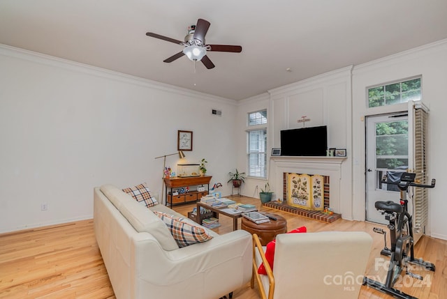 living room featuring ceiling fan, light hardwood / wood-style flooring, a brick fireplace, and ornamental molding