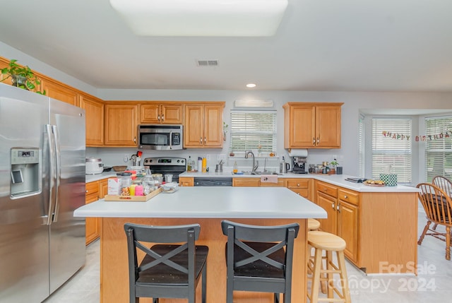 kitchen featuring appliances with stainless steel finishes, a kitchen bar, sink, a kitchen island, and light tile patterned flooring