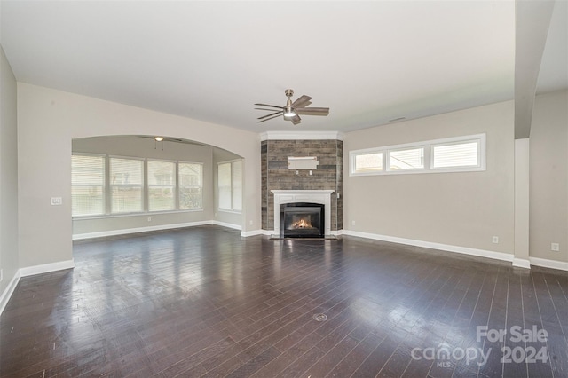 unfurnished living room featuring ceiling fan, a fireplace, dark wood-type flooring, and a healthy amount of sunlight