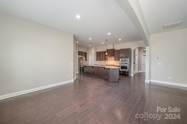 kitchen featuring appliances with stainless steel finishes, dark wood-type flooring, a kitchen bar, a kitchen island with sink, and sink