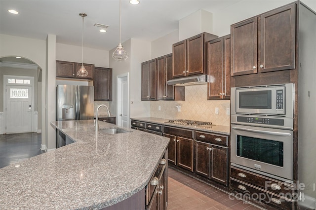 kitchen featuring a kitchen island with sink, sink, hanging light fixtures, appliances with stainless steel finishes, and dark brown cabinetry