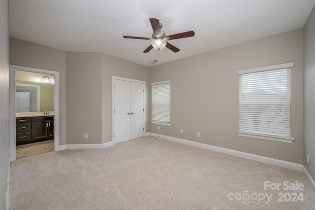 unfurnished bedroom featuring connected bathroom, a closet, ceiling fan, sink, and light colored carpet