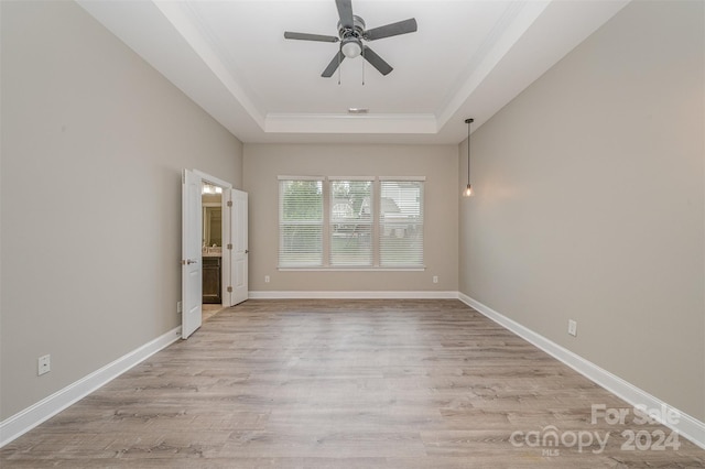 empty room featuring ceiling fan, light wood-type flooring, and a raised ceiling