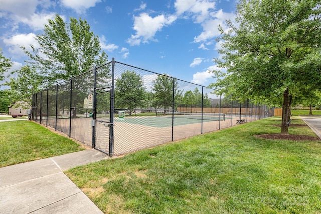view of tennis court featuring a lawn and fence