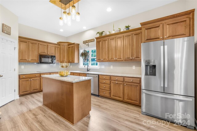 kitchen with sink, hanging light fixtures, light stone counters, a kitchen island, and appliances with stainless steel finishes