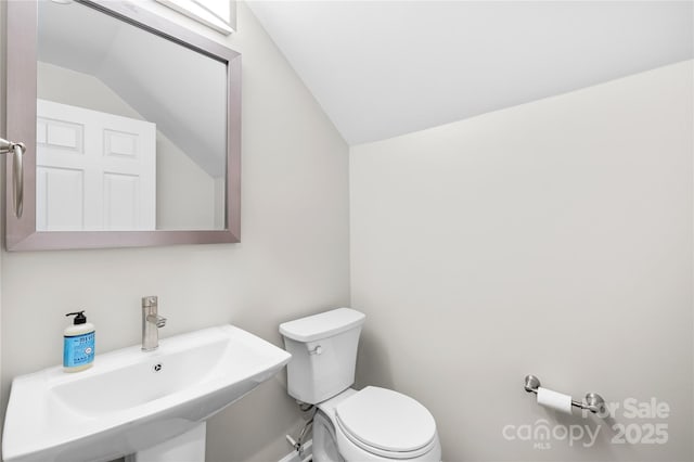 half bath with toilet, a sink, and lofted ceiling