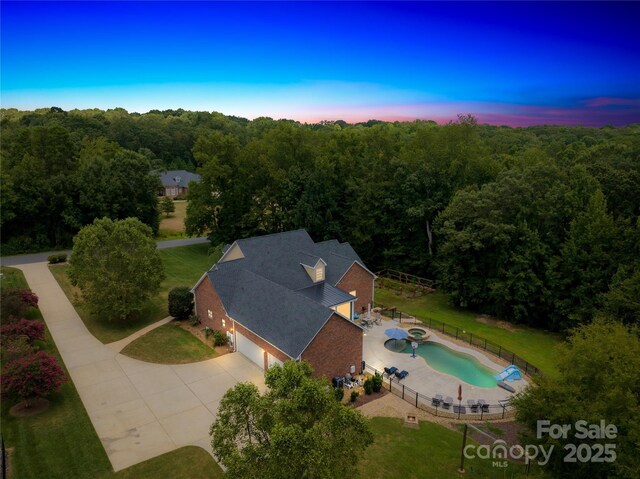 aerial view at dusk featuring a wooded view