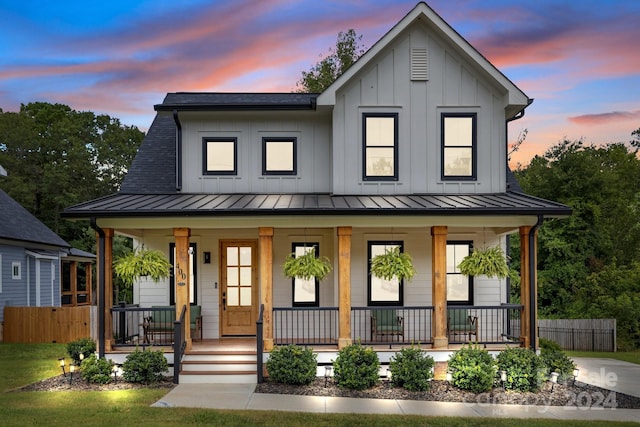 modern farmhouse style home with a standing seam roof, metal roof, covered porch, fence, and board and batten siding