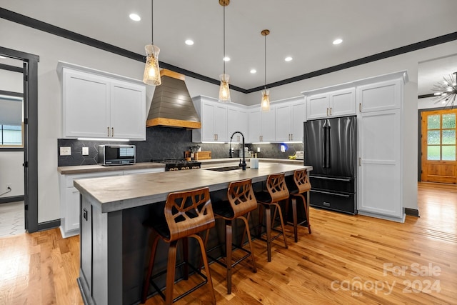 kitchen with high end refrigerator, white cabinets, premium range hood, pendant lighting, and a sink