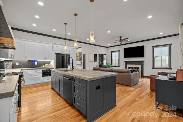 kitchen with freestanding refrigerator, white cabinetry, hanging light fixtures, and an island with sink