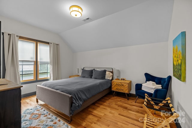 bedroom with light wood finished floors, visible vents, and vaulted ceiling