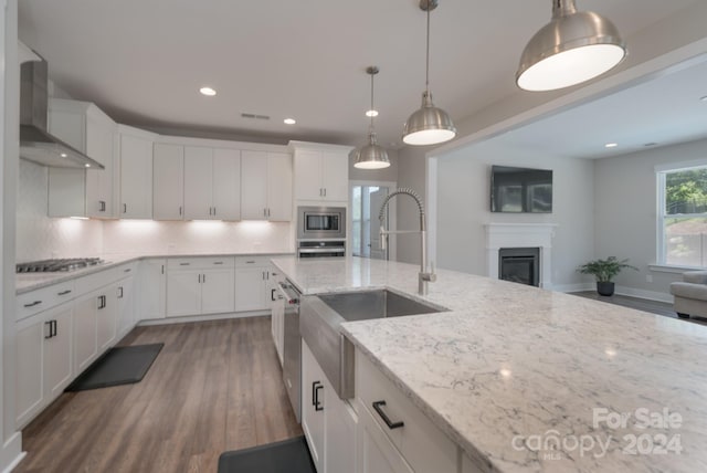 kitchen with appliances with stainless steel finishes, hardwood / wood-style floors, tasteful backsplash, light stone countertops, and wall chimney range hood