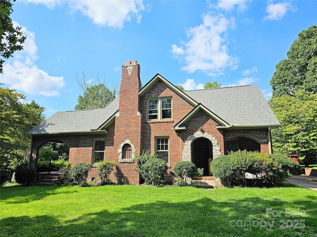 view of front of home with a front yard, brick siding, a chimney, and roof with shingles