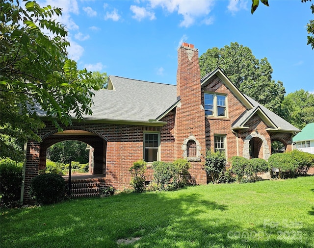 view of front of property with a shingled roof, a front yard, brick siding, and a chimney