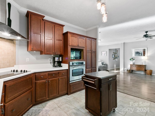 kitchen with ornamental molding, light wood-type flooring, wall chimney exhaust hood, ceiling fan, and black appliances