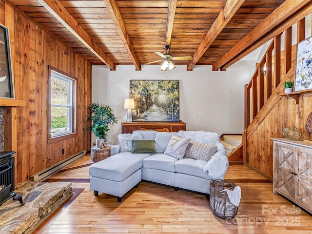 living room featuring a wood stove, light wood-style floors, a baseboard radiator, and beamed ceiling