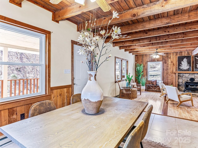 dining area featuring beam ceiling, a baseboard radiator, a ceiling fan, wooden walls, and wooden ceiling