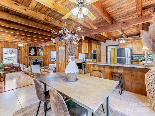 dining space featuring wooden walls, wood ceiling, a fireplace, and a ceiling fan