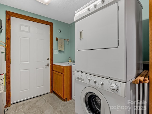 washroom with a sink, stacked washer and dryer, a textured ceiling, and cabinet space