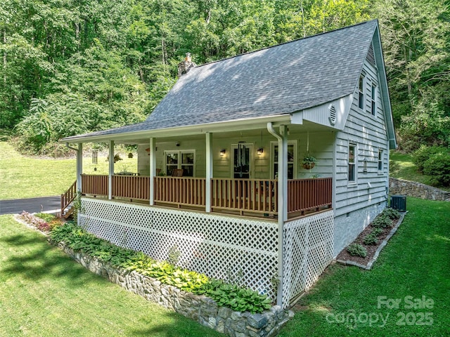 view of front of home with central air condition unit, covered porch, roof with shingles, a front lawn, and a chimney