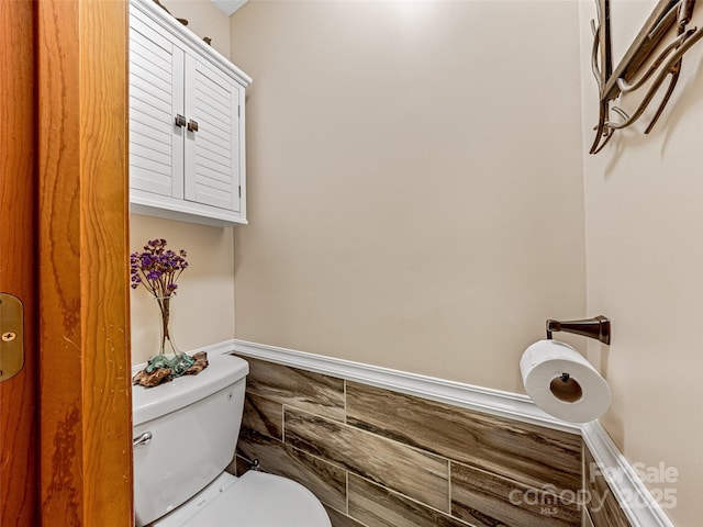 bathroom featuring wainscoting, tile walls, and toilet