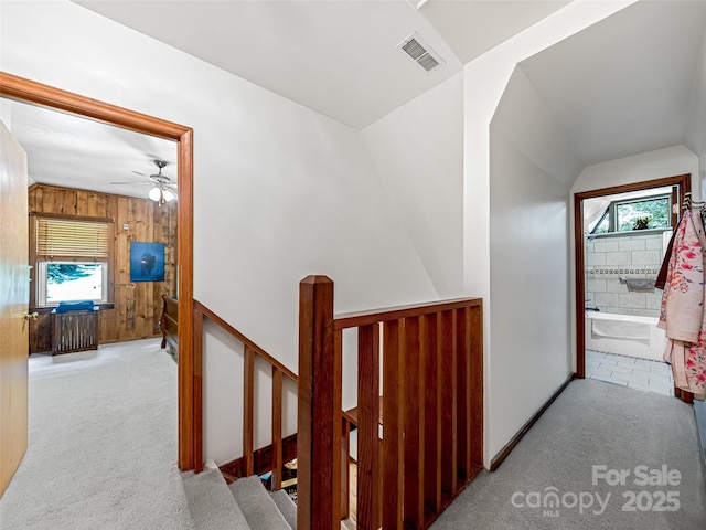 corridor featuring carpet floors, visible vents, wood walls, and an upstairs landing