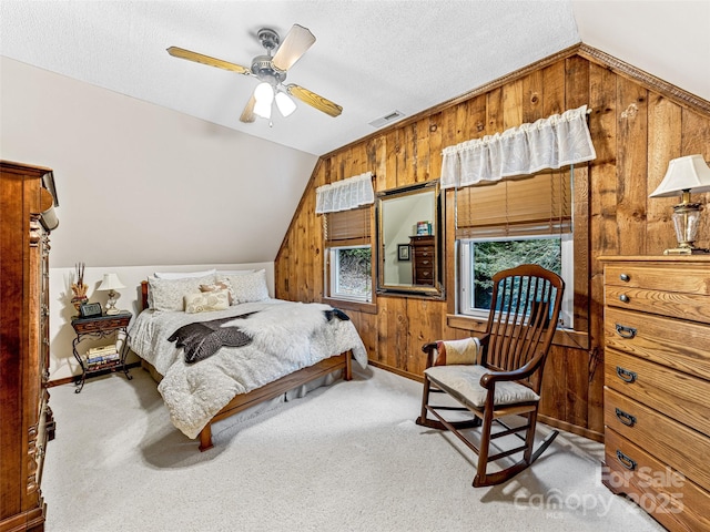 carpeted bedroom featuring lofted ceiling, a textured ceiling, visible vents, and wooden walls